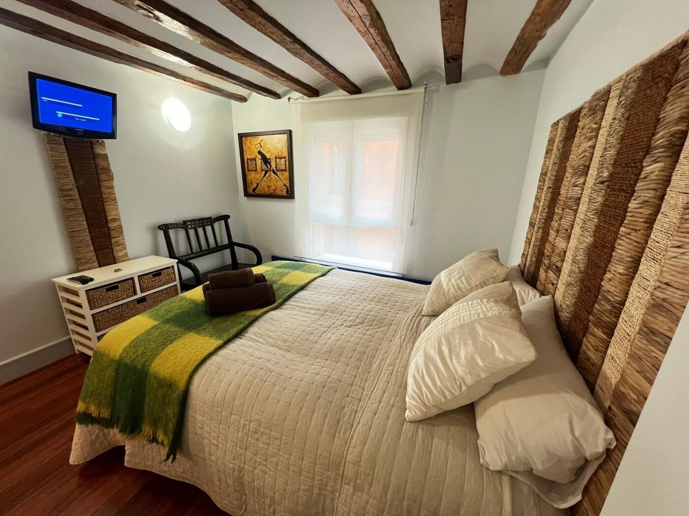 Un dormitorio con cama, televisor, una silla, escritorio con espacio de almacenamiento y ventana.