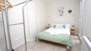 A bedroom with a bed, a radiator, a wall-mounted artwork, and a wooden nightstand. - EL RINCÓN DE LA MERCED I (Logroño)