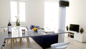 A modern living room with a dining table, two white bar stools, a sofa, a television, and a sign that reads 'Bienvenue'. - EL RINCÓN DE LA MERCED I (Logroño)