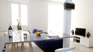 Un salon moderne comprenant une table à manger, deux tabourets de bar blancs, un canapé, un téléviseur et un panneau indiquant « Bienvenue ».