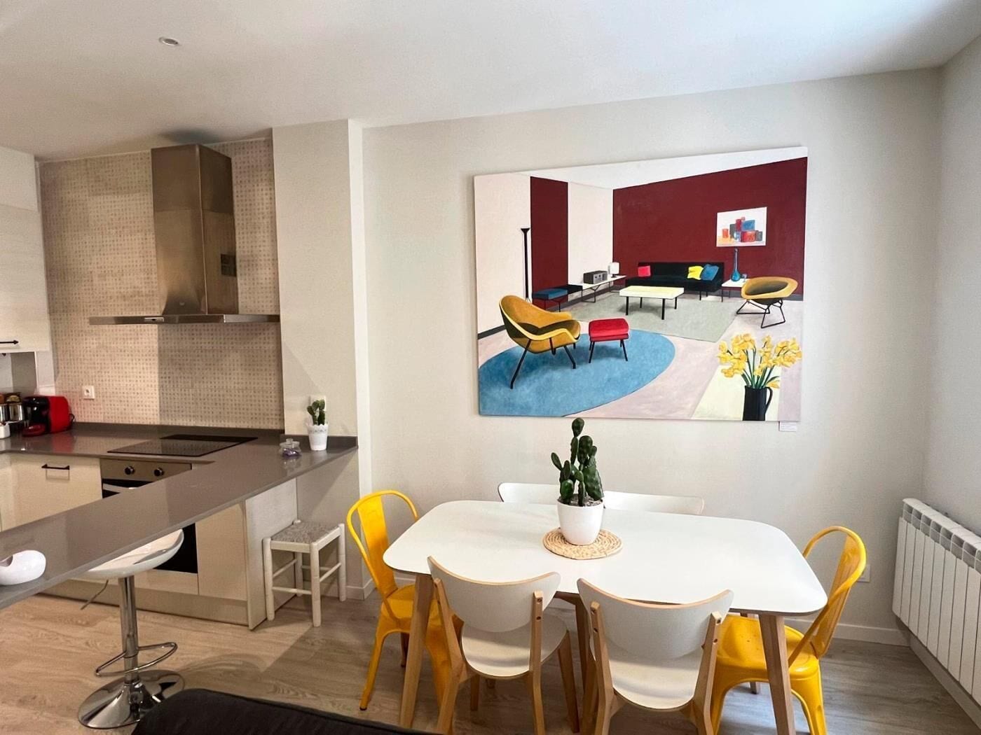 Een moderne keuken met een inbouwfornuis, een eethoek met een witte tafel en gele stoelen, en een woonkamer met een bank en salontafel.