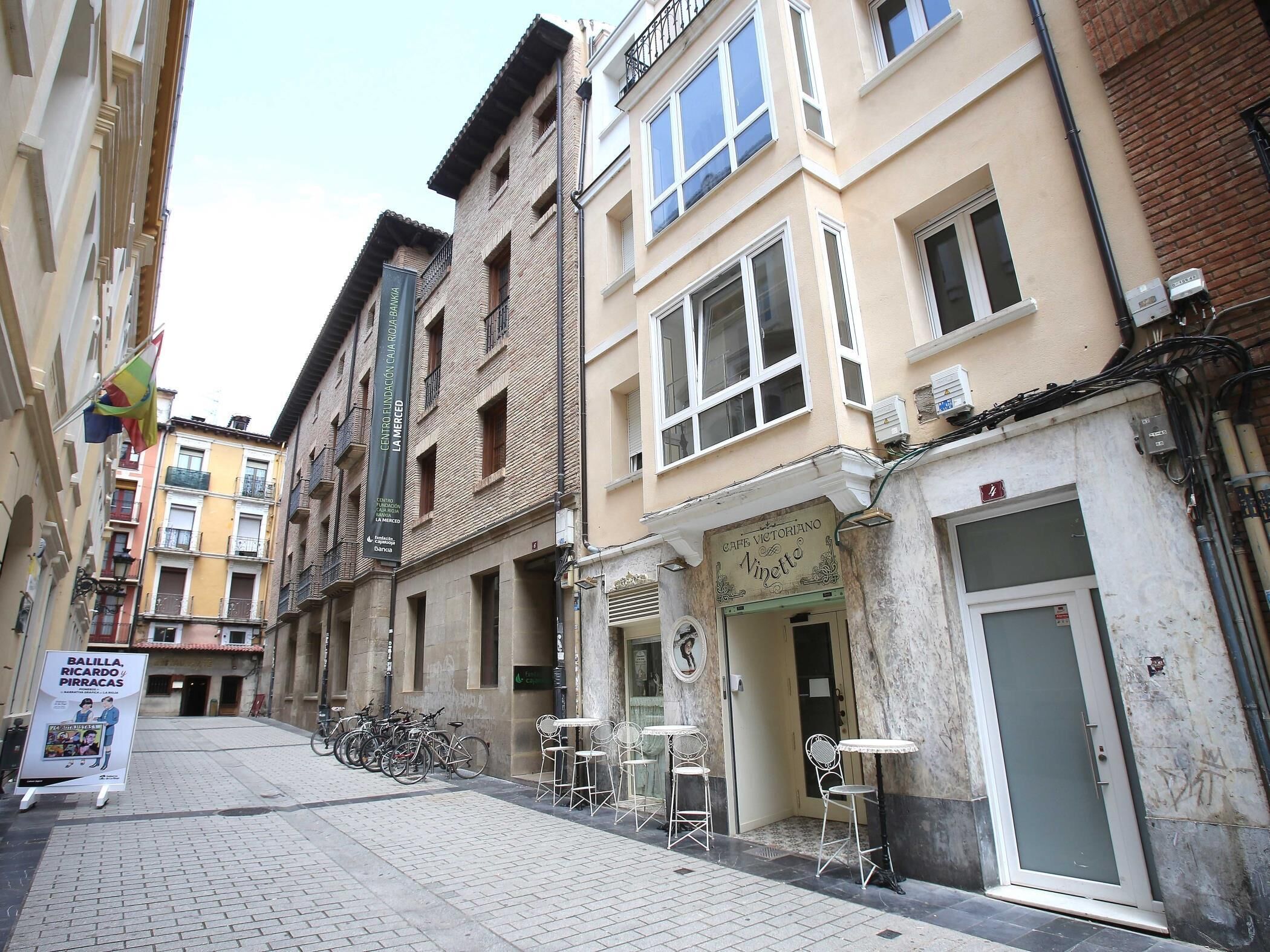 Een smalle straat met gebouwen, een café en terrasjes.