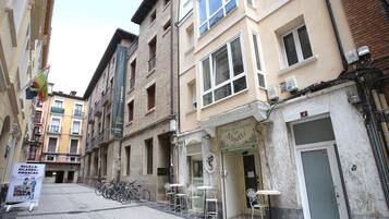 Een smalle straat met gebouwen, een café en terrasjes.
