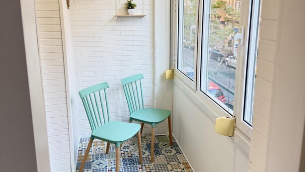 A corner room with two chairs, a white brick wall, a window with a view of buildings, and a tiled floor. - Rioja Centro 3 habitaciones (Logroño)