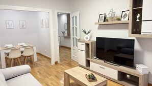 A modern living room with a sofa, coffee table, TV, and a dining area with chairs and a table. - Rioja Centro 3 habitaciones (Logroño)