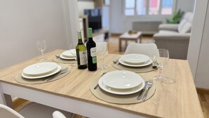 A dining table set with plates, cutlery, and wine bottles in a modern, well-lit room with a sofa and a window in the background. - Rioja Centro 3 habitaciones (Logroño)