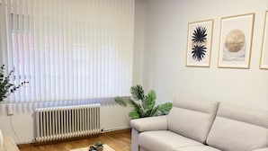 A living room with a sofa, a coffee table, a radiator, and a window with blinds. - Rioja Centro 3 habitaciones (Logroño)