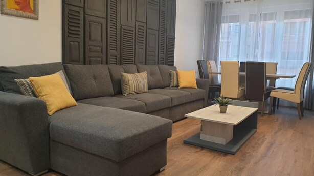 En moderne stue med en hjørnesofa, et sofabord og et spiseområde med stole og et bord.