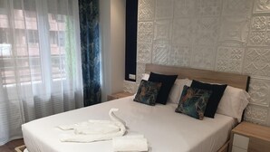 Et hotelværelse med en stor seng, en sengegavl med detaljerede mønstre, et natbord og et vindue med let gardin.