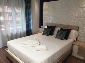 Een hotelkamer met een groot bed, een hoofdbord met ingewikkelde patronen, een nachtkastje en een raam met dunne gordijnen.