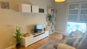 A modern living room with a flat-screen TV, white storage units, a grey sofa, and a large window with blinds. - Santiago Tower Views (Logroño)
