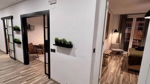 Un pasillo de hotel con suelo de madera, puertas con marcos negros y pequeñas plantas decorativas en las paredes.
