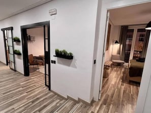 Un pasillo de hotel con suelo de madera, puertas con marcos negros y pequeñas plantas decorativas en las paredes.