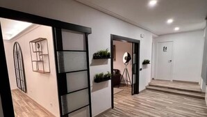 Un pasillo con suelo de madera, una puerta corredera, un estante empotrado con plantas y una puerta con un cartel.