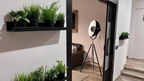 Un pasillo con estanterías negras que sostienen plantas en macetas, un trípode con una luz y una puerta que da a otra habitación.