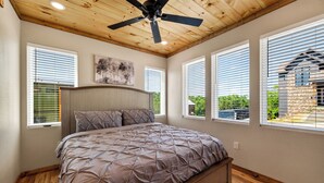 Ein Schlafzimmer mit Bett, Deckenventilator und großen Fenstern.