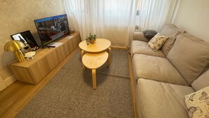Ein Wohnzimmer mit einer Couch, einem Fernseher, einem kleinen Tisch und einer Pflanze.