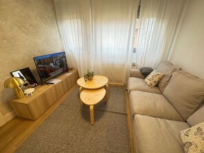 Ein Wohnzimmer mit einer Couch, einem Fernseher, einem kleinen Tisch und einer Pflanze.