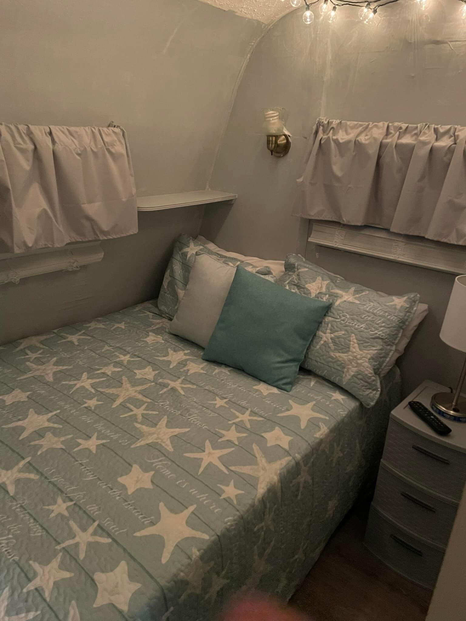 A small, cozy bedroom with a bed, pillows, a nightstand, and a lamp.