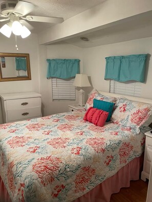 A bedroom with a bed, a nightstand, a dresser, a ceiling fan, and a window with curtains.