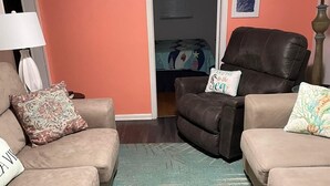 Ein Wohnzimmer mit zwei Sofas, einem gemusterten Teppich, einer Uhr und gerahmten Bildern an der Wand.