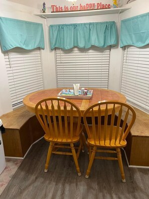 A corner dining area with two wooden chairs, a round wooden table, and a tray with a book and a cup.
