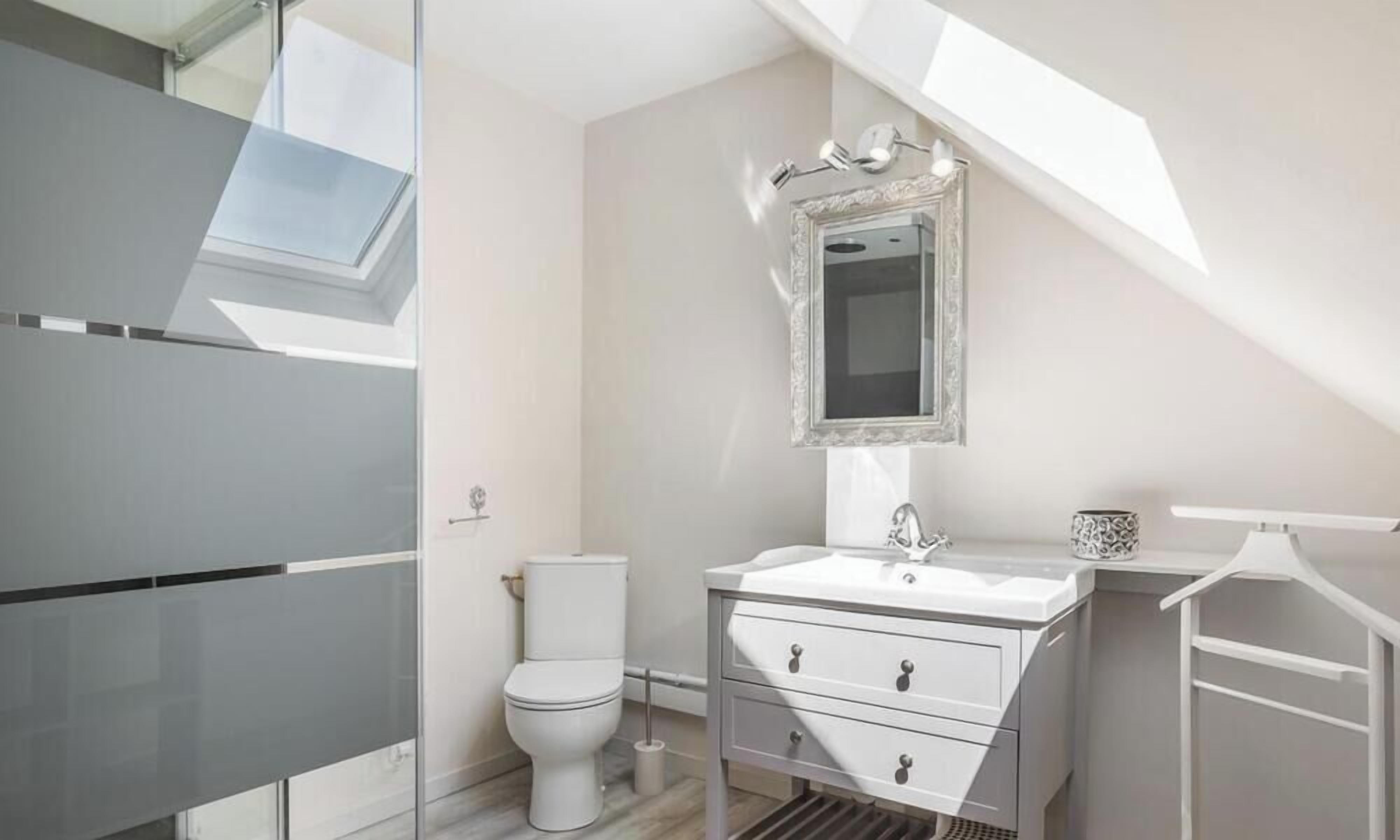 Een moderne badkamer met dakraam, een wit toilet, een wastafel met spiegel en een ophangrek voor handdoeken.