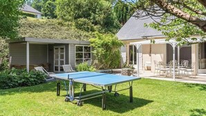 A ping pong table in a backyard with a covered seating area and a house in the background. - Gîtes de France® - La Margautine (VEULETTES SUR MER)