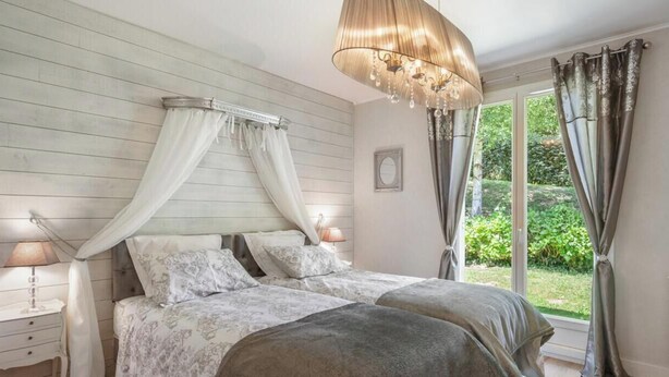 A bedroom with a canopy bed, bedside lamps, and a view of greenery outside. - Gîtes de France® - La Margautine (VEULETTES SUR MER)