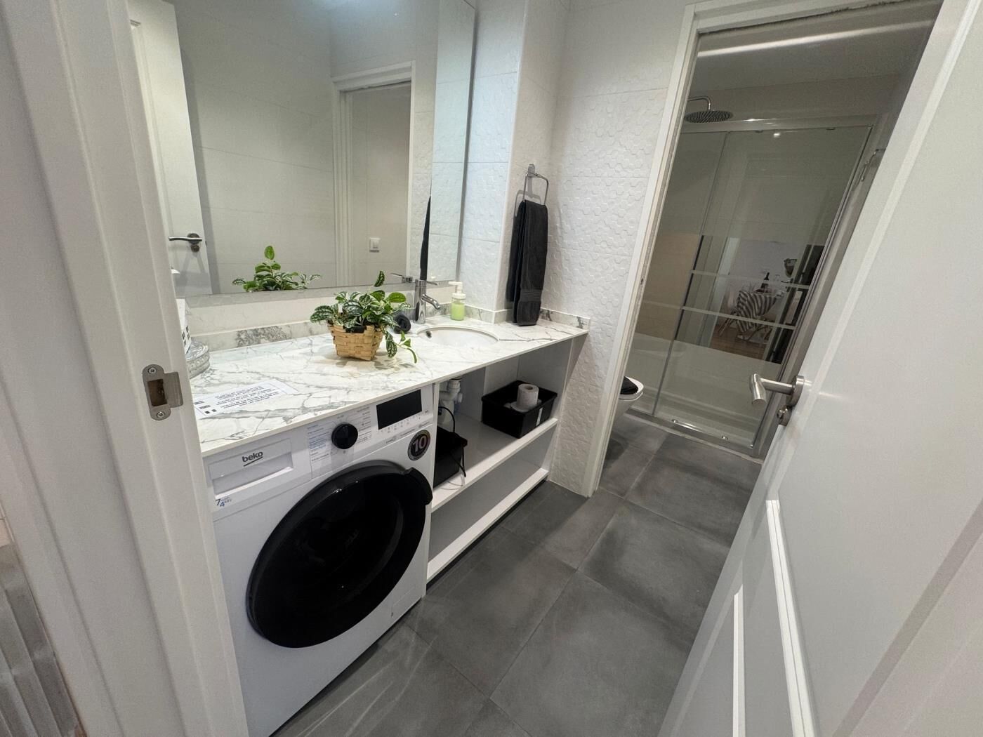 A modern bathroom with a marble sink, a washing machine, and a glass shower enclosure.
