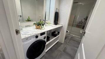 A modern bathroom with a marble sink, a washing machine, and a glass shower enclosure.