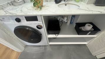 Un lavadero pequeño con lavadora, lavamanos y un espacio de almacenamiento.