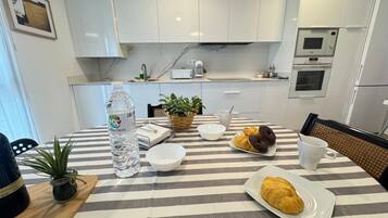 Una cocina moderna con armarios blancos, un mantel a rayas, una botella de agua, un plato de croissants y una taza de café.