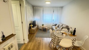 A modern living room with a sofa, a dining table with chairs, a TV, and a small side table. - PRECIOSOS APARTAMENTOS RIOJALAND EN LARDERO (Lardero)