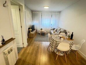 Ein modernes Wohnzimmer mit einer Couch, einem Esstisch mit Stühlen, einem Fernseher und einem kleinen Beistelltisch.