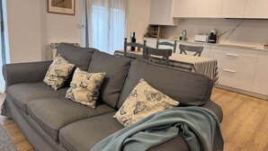 A modern living room with a grey sofa, patterned cushions, a dining area with a striped tablecloth, and a kitchen with white cabinets. - PRECIOSOS APARTAMENTOS RIOJALAND EN LARDERO (Lardero)