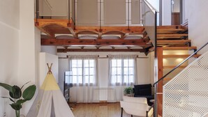 Une pièce de style « loft », dotée d’un escalier en bois, offrant une vue sur l’extérieur et comprenant un petit coin salon avec un canapé et un fauteuil.