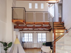 A loft-style room with a wooden staircase, a view of the outdoors, and a small seating area with a sofa and a chair.