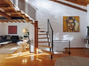 A modern interior with a wooden staircase, a painting on the wall, and a sofa in a well-lit room.