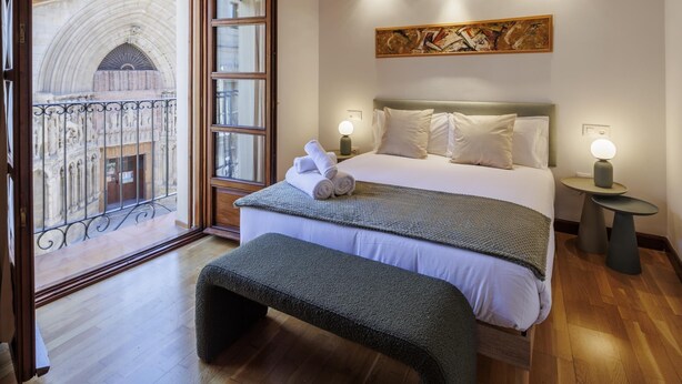 Une chambre d’hôtel avec un lit, une banquette, des tables de chevet et une vue sur un bâtiment historique.