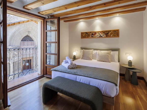 A hotel room with a bed, bench, bedside tables, and a view of a historic building.
