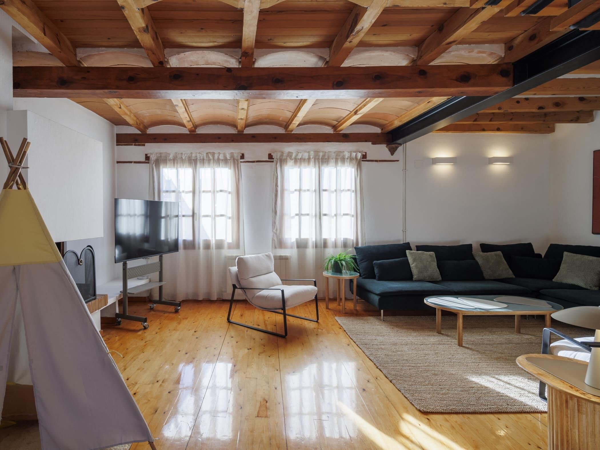 Un salon avec un plafond en bois, un canapé, un téléviseur et une structure ressemblant à une tente.