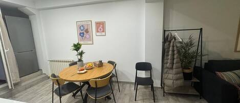 A modern living room with a round wooden table, two chairs, a black sofa, a radiator, and a potted plant.