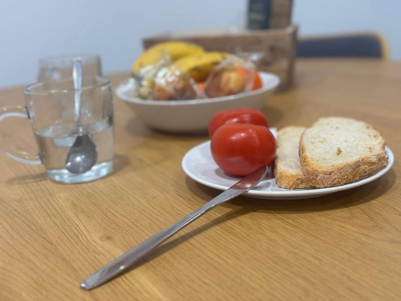 Una mesa de comedor con un plato de comida, un vaso de agua y una cuchara.