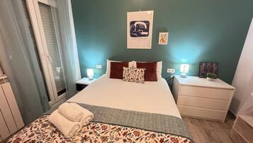 Een slaapkamer met een bed, twee nachtkastjes, een kunstwerk aan de muur en een raam met gordijnen.