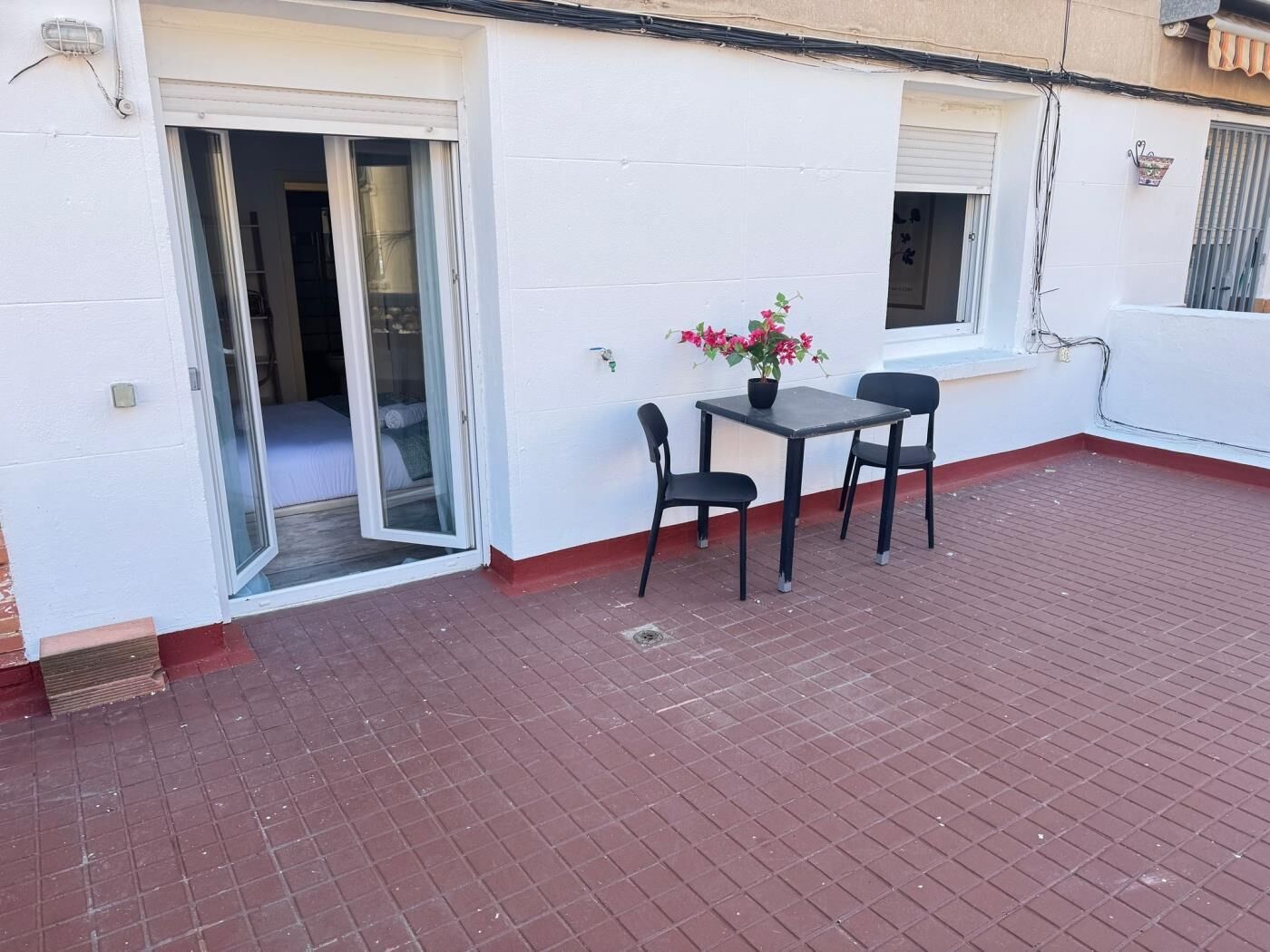 A patio with a table and chairs, a potted plant, and a sliding glass door leading to a room.