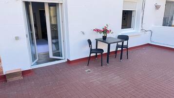 A patio with a table and chairs, a potted plant, and a sliding glass door leading to a room.