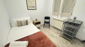 A bedroom with a bed, a chair, a small table with a plant, a radiator, and a wall-mounted picture.