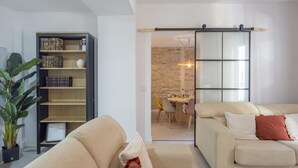 A modern living room with a beige sofa, a bookshelf, and a sliding glass door leading to a dining area. - CASA BOUTIQUE SAN JUAN (LOGROÑO)