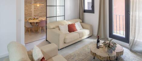 A modern living room with a sofa, a dining area, and a sliding glass door to the outside.